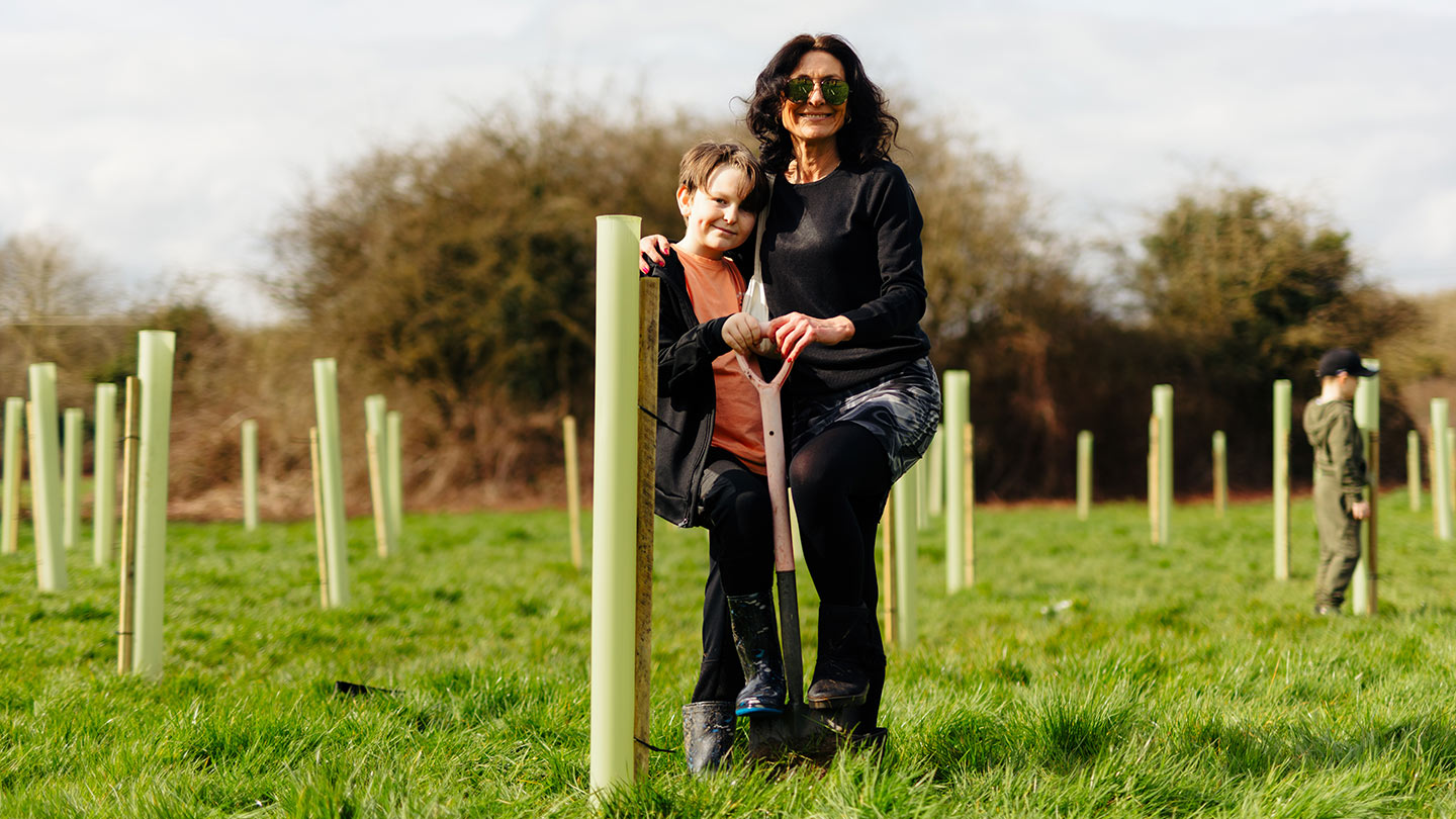 People posing for photo amongst newly-planted trees in grassy field.