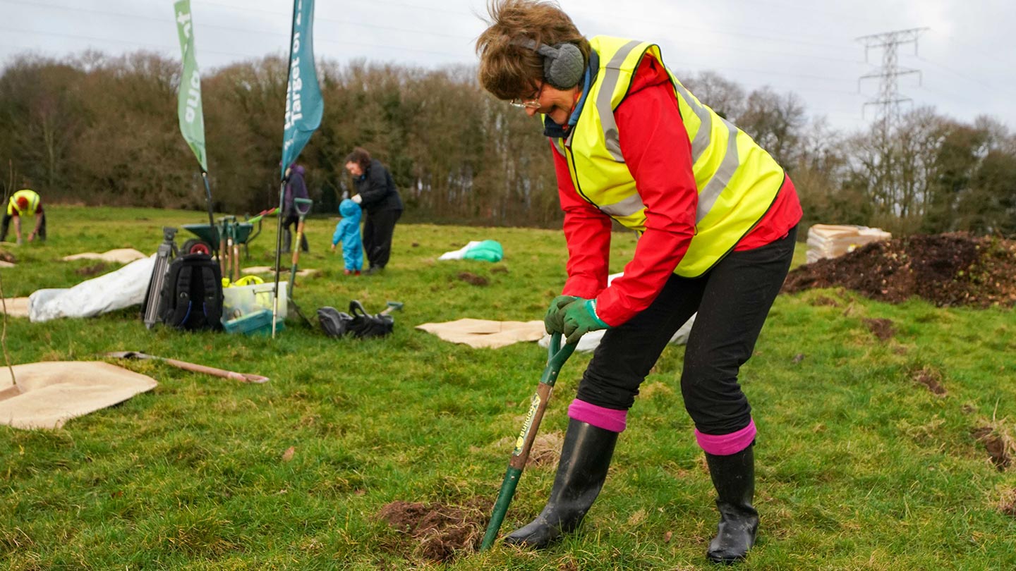 Person in high-vis jacket digging hole for tree planting with shovel.