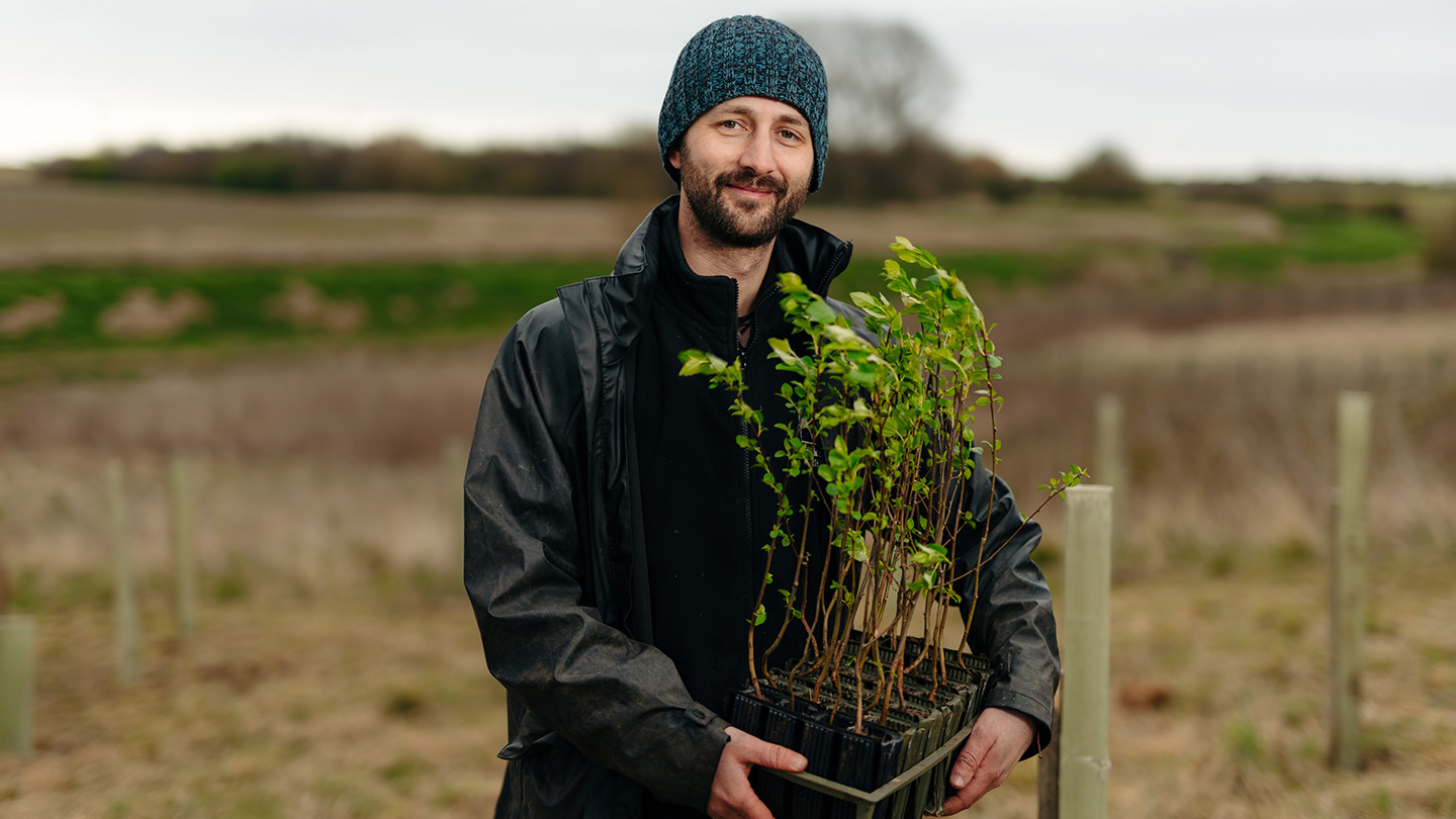 Person holding tree sapling box with marshy landscape behind.